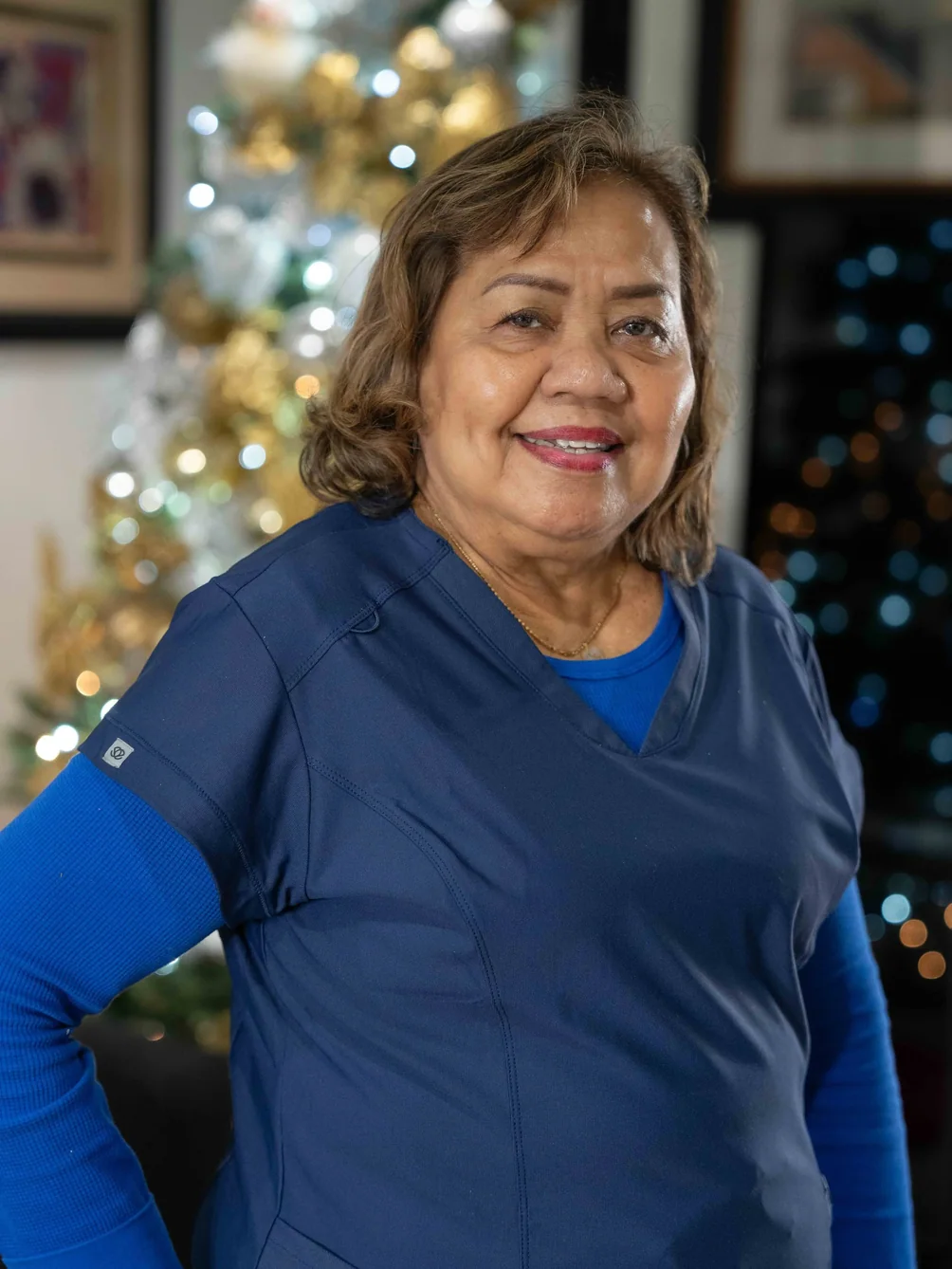 Professional caregiver in navy scrubs smiling warmly with holiday decorations
