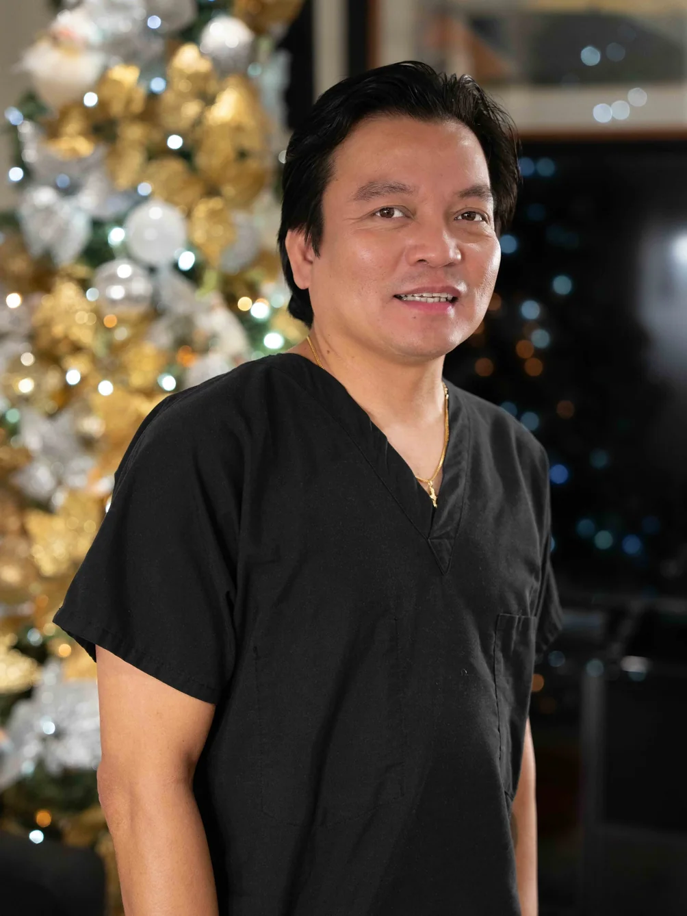 Smiling caregiver in medical scrubs standing in front of festive Christmas tree