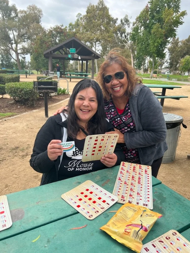 Two women enjoying a game of bingo together at an outdoor park table