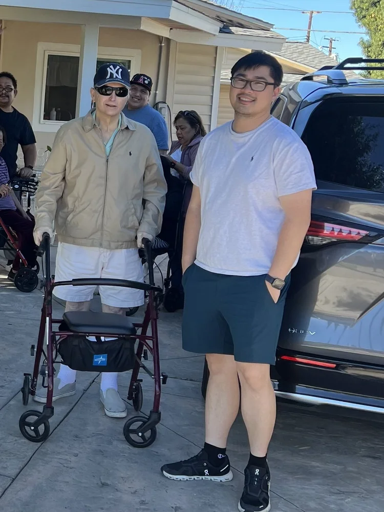 Caregiver and elderly resident with mobility walker standing together outside