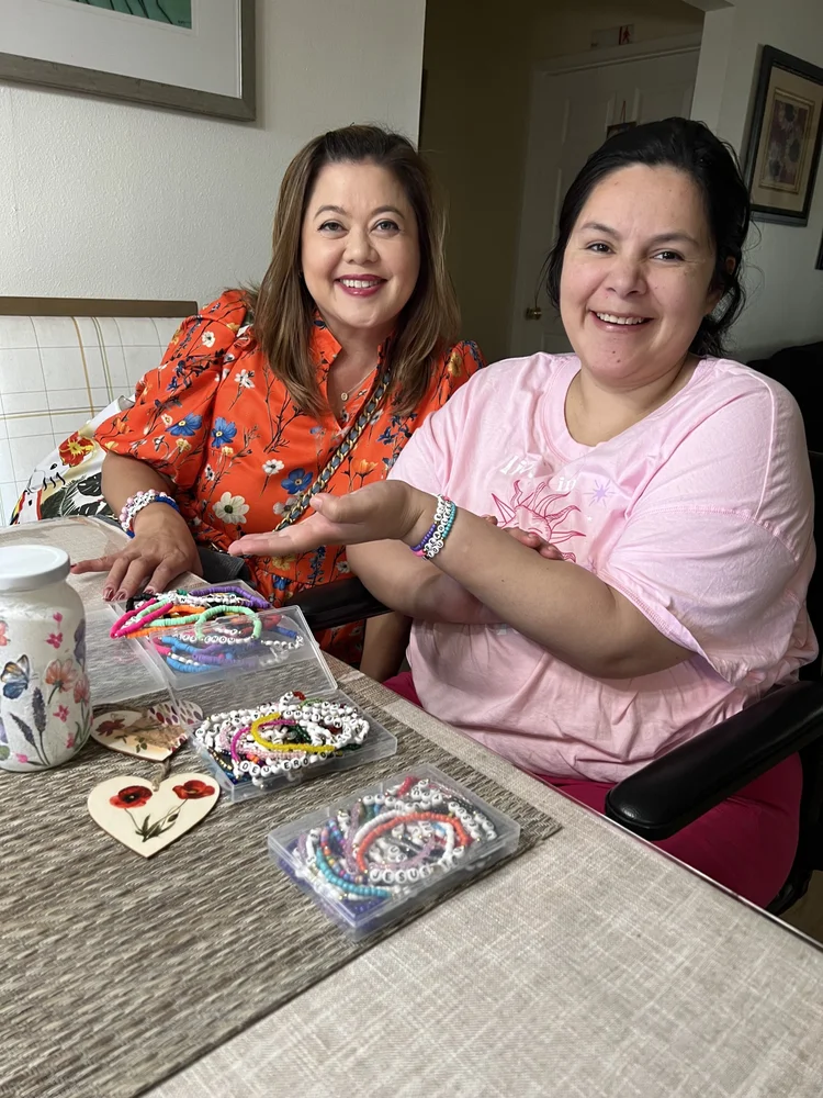 Two women smiling while making beaded bracelets together at a table